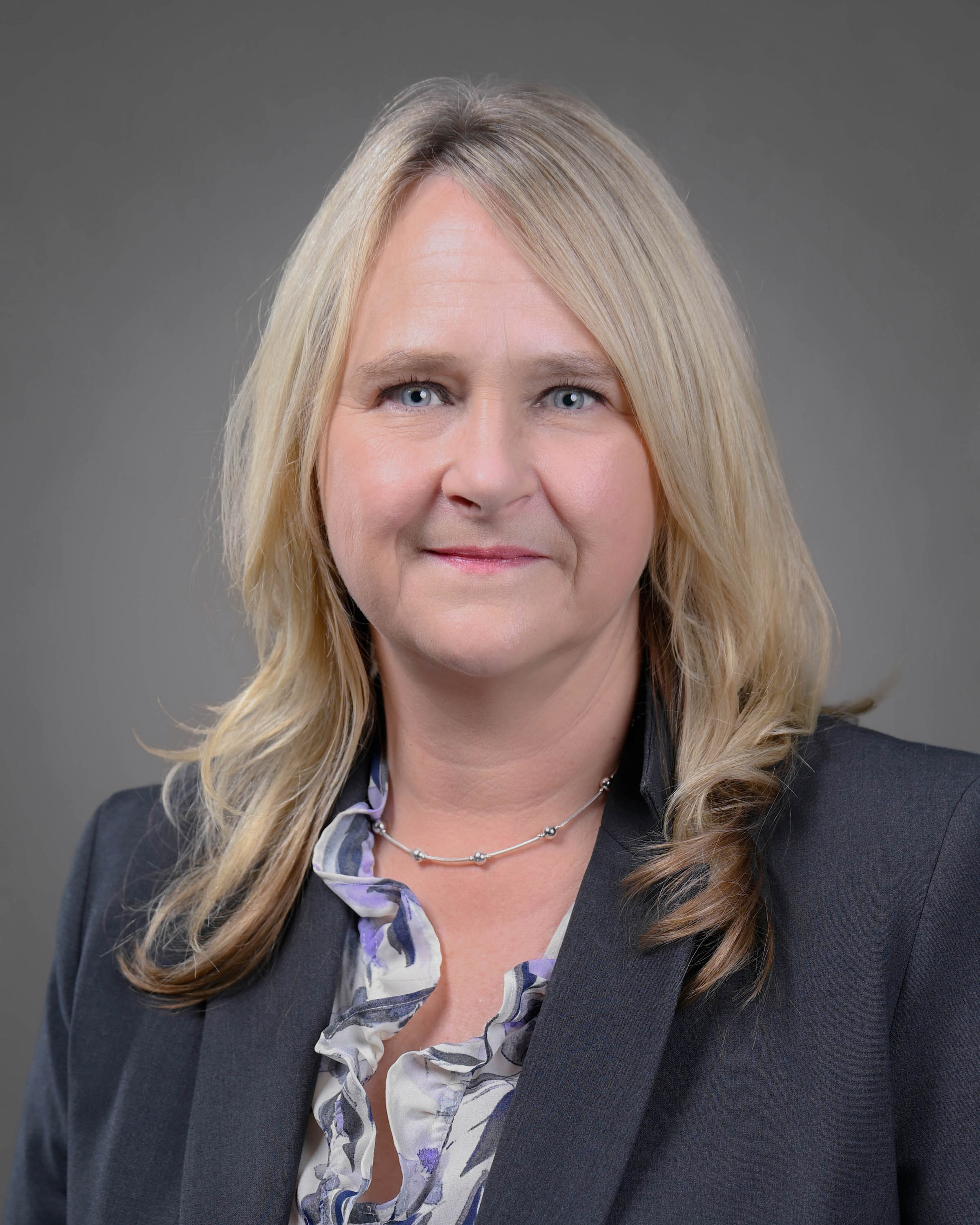 Blonde woman with a blue jacket on and floral print shirt.